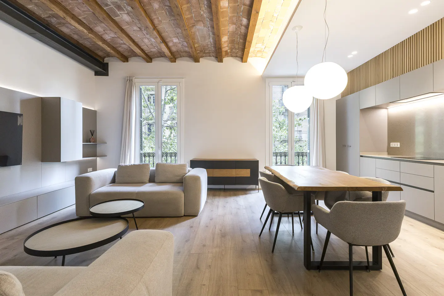 Open-concept living space with exposed brick ceiling, light wood floors, and modern furniture. Large windows offer natural light.