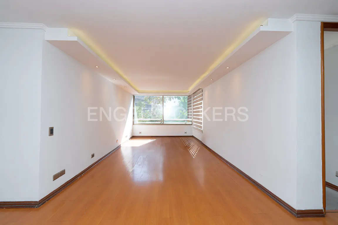 Bright, empty room with hardwood floors and white walls. A large window lets in natural light. Ceiling has recessed lighting.