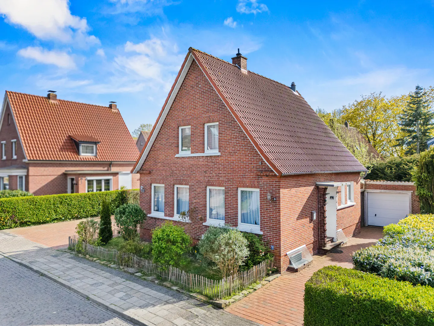 Two-story brick house with a red tile roof, white trim, and a detached garage on a sunny day.
