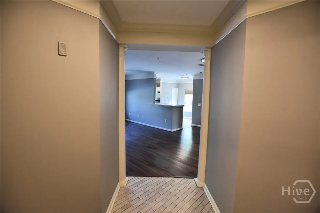A hallway with beige walls leads to a living room with dark wood floors and gray walls.