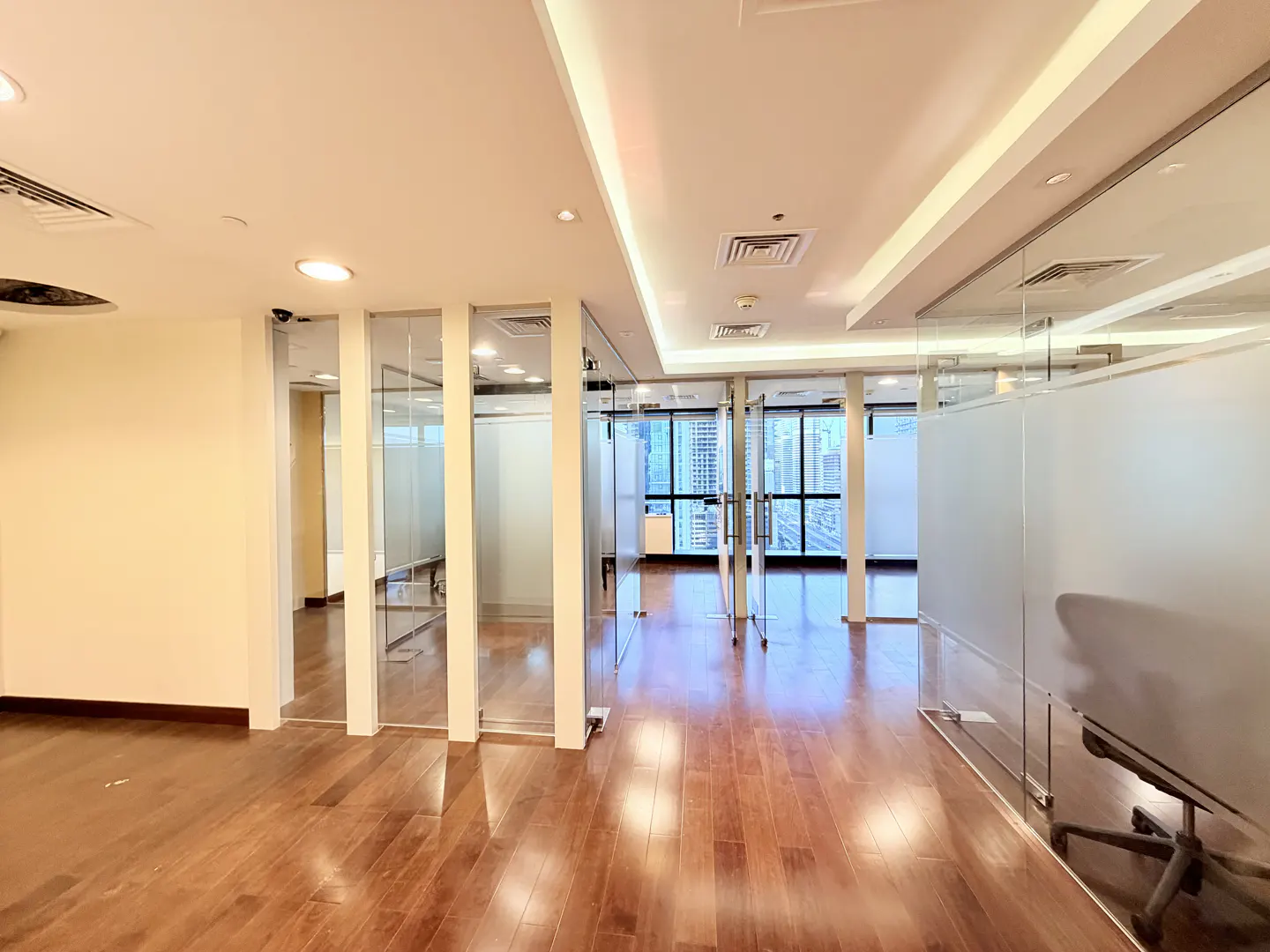 Empty office space with wood floors, glass walls, and a view of a city skyline.
