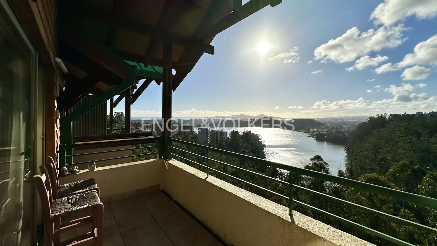 Balcony view of a lake on a sunny day. Two chairs sit on the balcony with a green railing. The sun shines over the water.