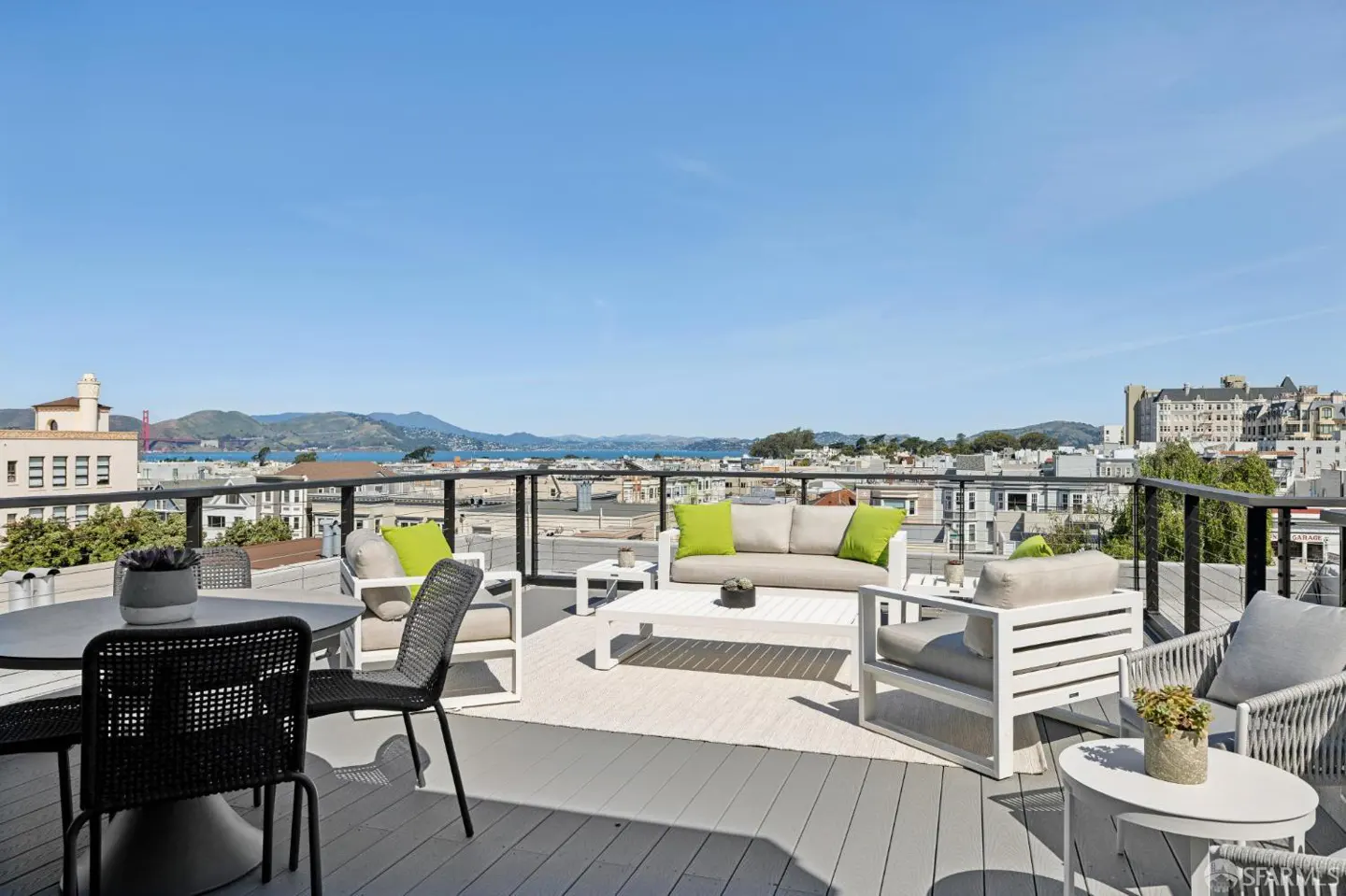 Rooftop patio with outdoor furniture, including a sofa, chairs, and a table, overlooking a city skyline and the Golden Gate Bridge.