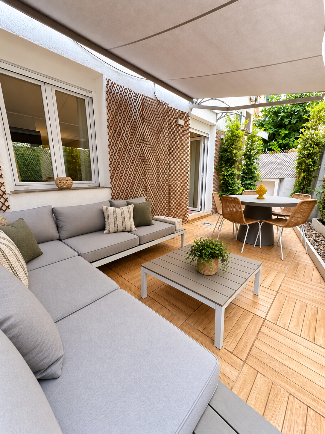 Modern outdoor patio with a large grey sectional sofa, coffee table, and dining set under a retractable white awning. [AI-generated text]