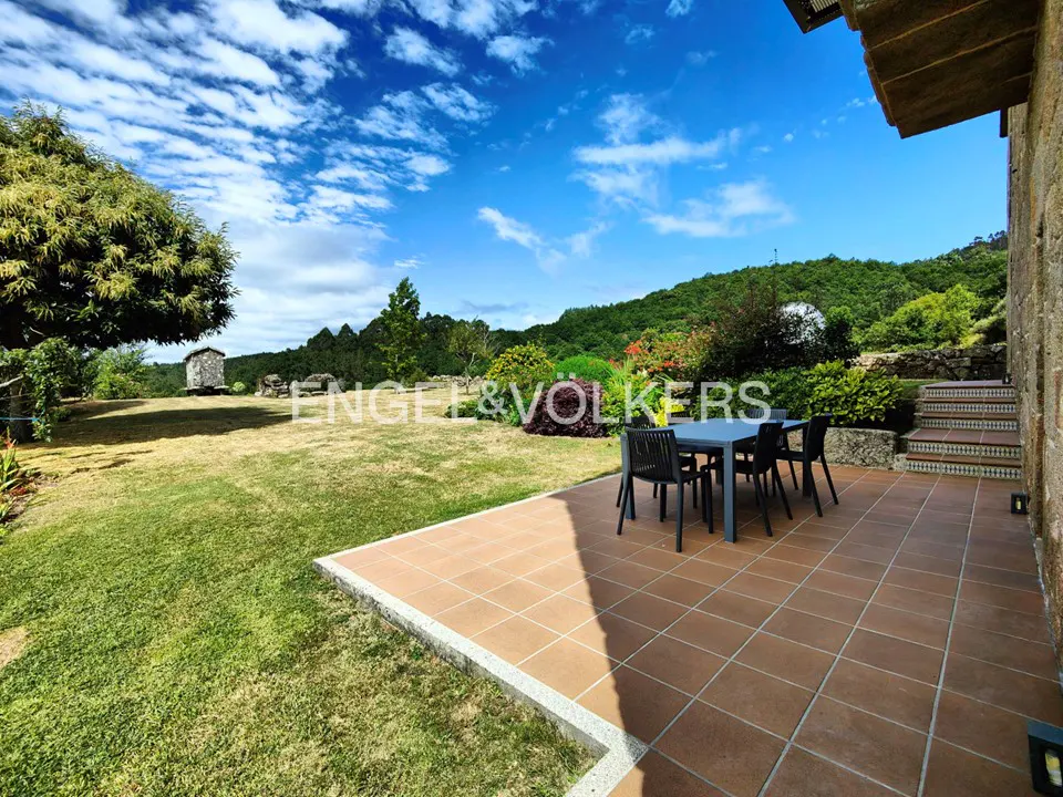 Outdoor patio with table and chairs, green lawn, and blue sky. Lush green hills in the background.