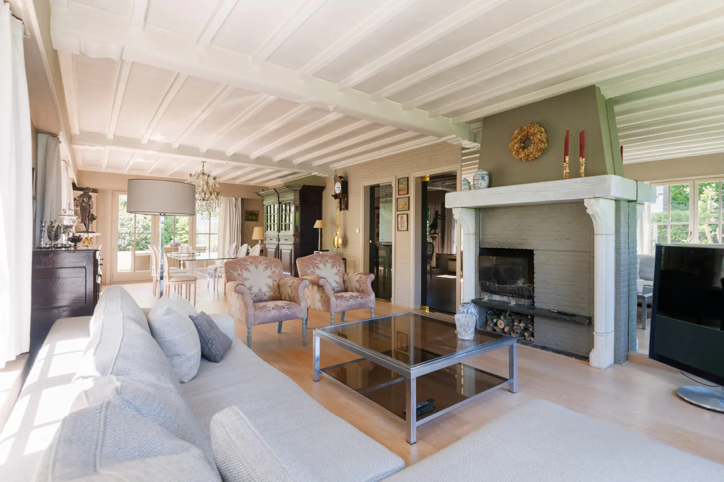 Spacious living room with a white sofa, glass coffee table, two patterned armchairs, and a green fireplace with a wreath.