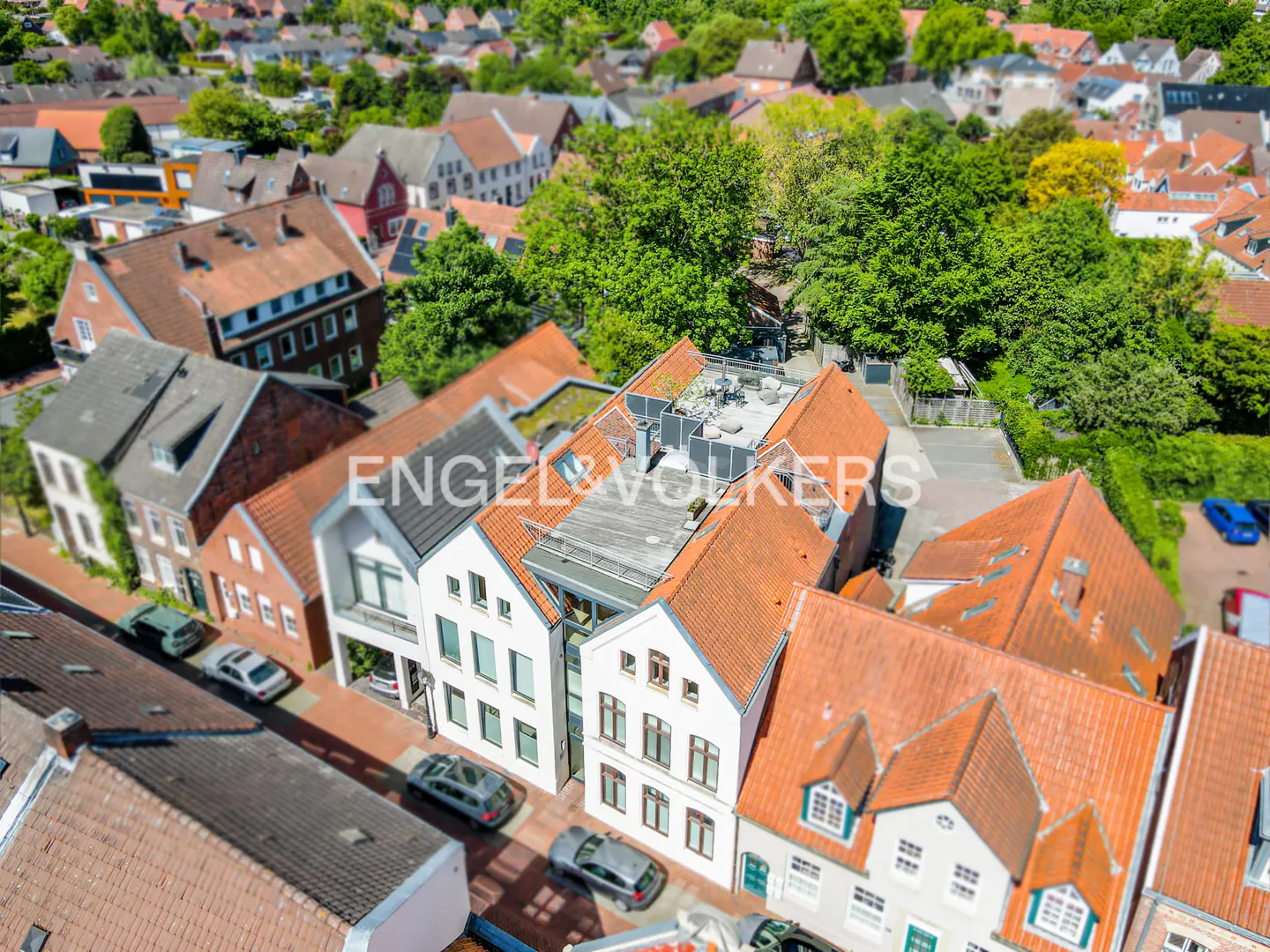 Aerial view of a European town with red-tiled roofs, white buildings, and green trees. The Engel & Volkers logo is visible.