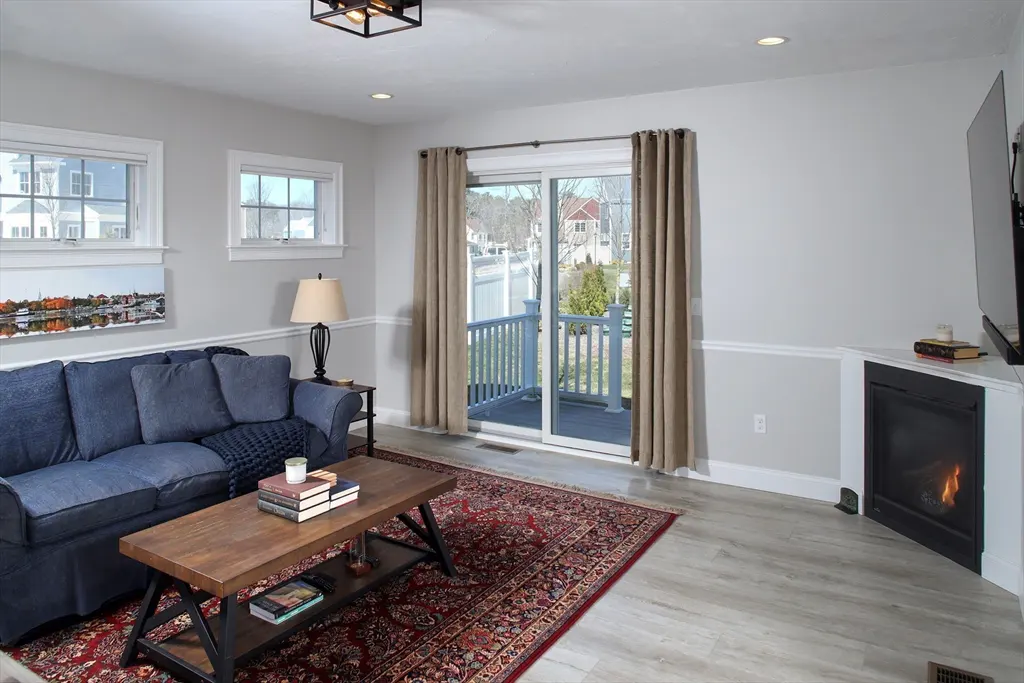 Living room with gray walls, a blue sofa, a wood coffee table on a red rug, and a fireplace with a TV above it.