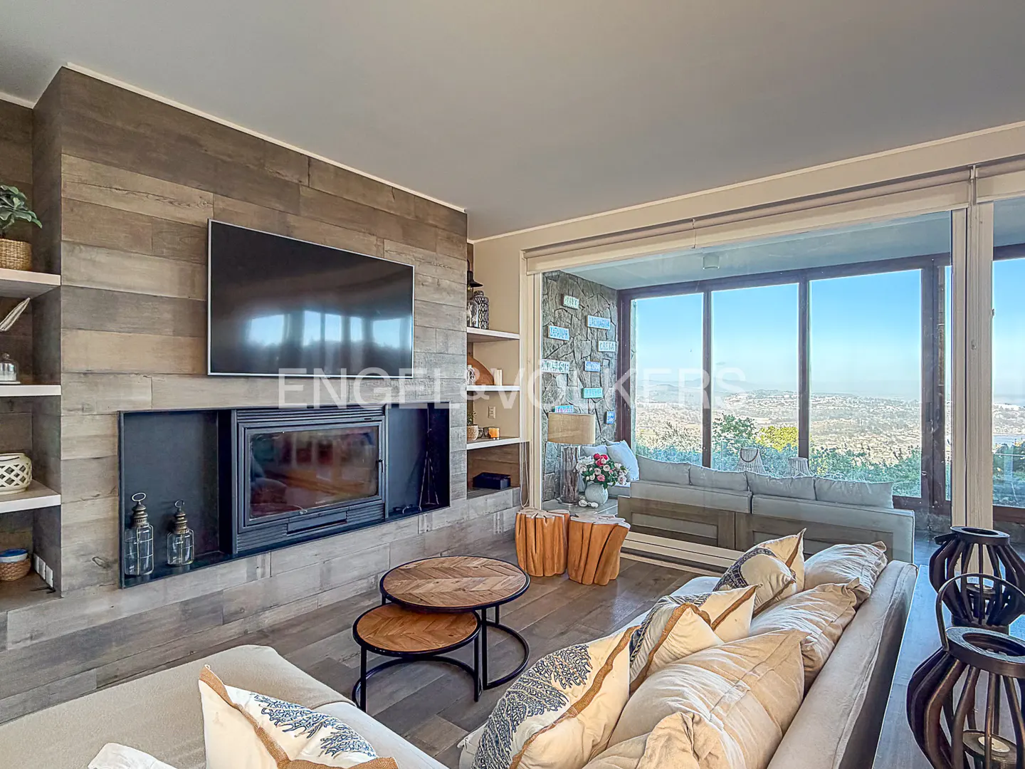 Living room with a fireplace, TV, and a large window with a view of the city. The room is decorated in neutral colors.