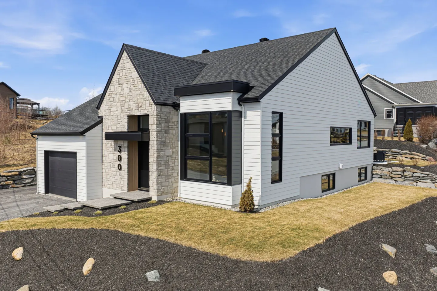 Modern two-story home with white siding, stone accents, black trim, and a dark gray roof on a sunny day.
