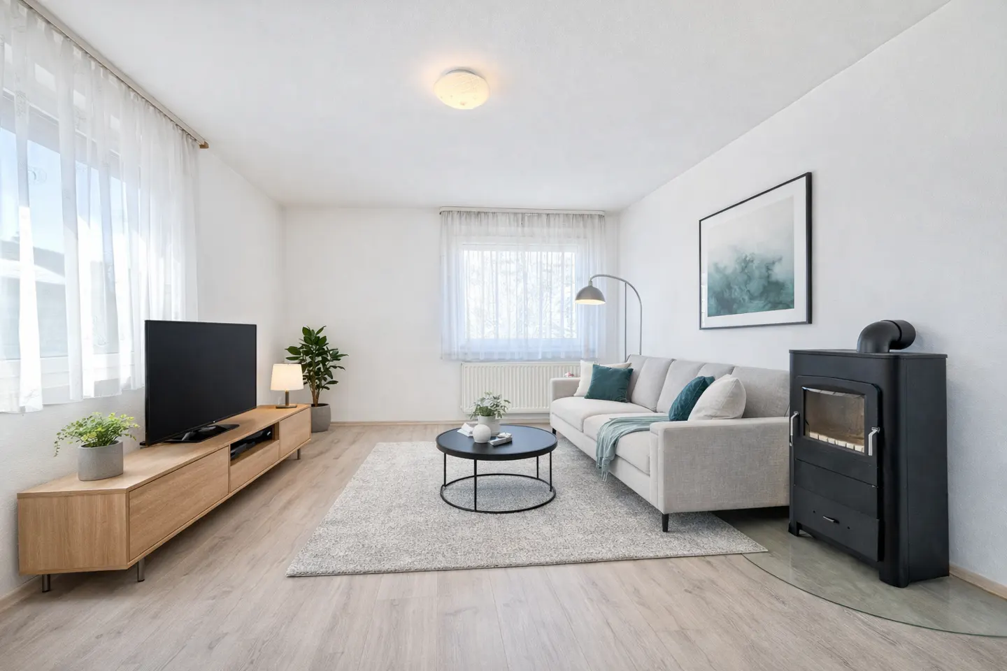 Bright living room with a gray sofa, black stove, wood TV stand, and a round coffee table on a light gray rug.