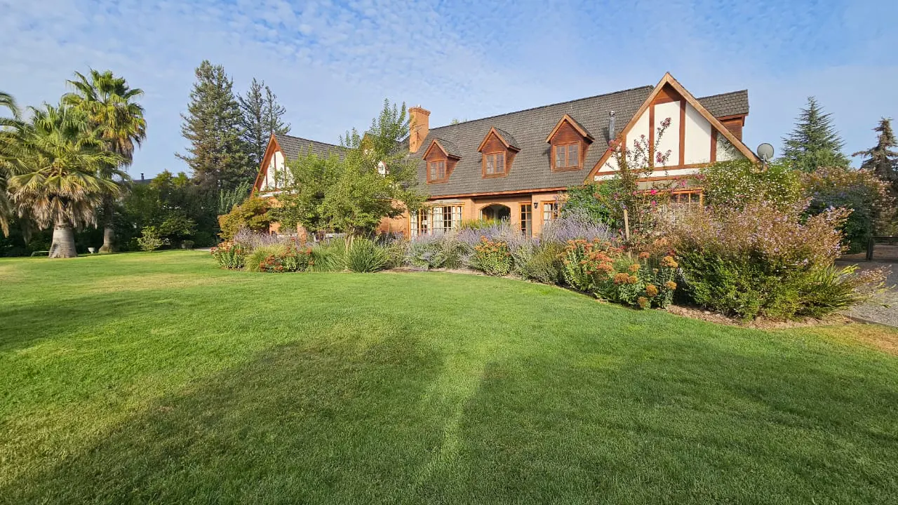 A two-story Tudor-style house with a large green lawn and landscaping under a blue sky.