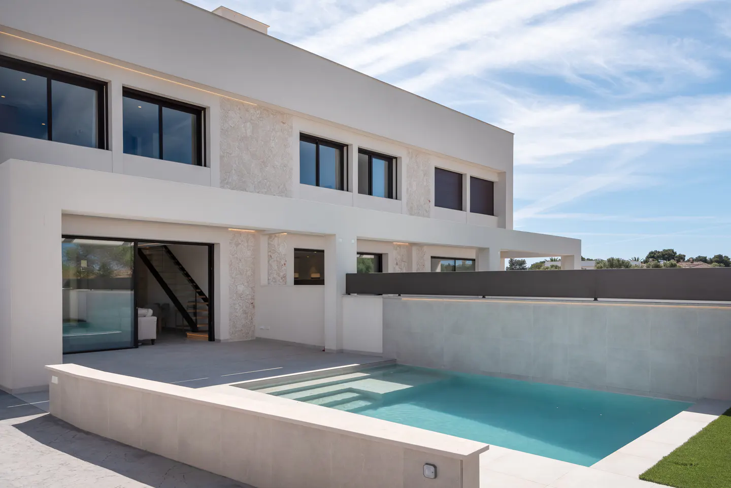 Modern white two-story house with a pool. Black framed windows and sliding glass doors. Blue sky background.