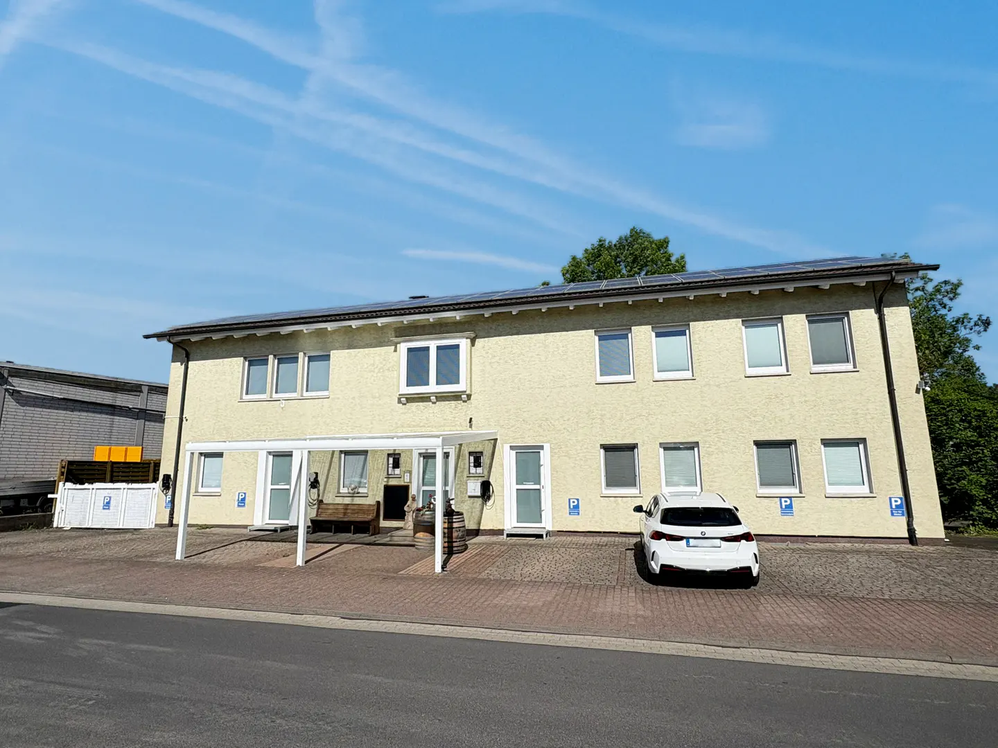 Two-story yellow building with white trim and solar panels. A white car is parked in front. Blue sky.