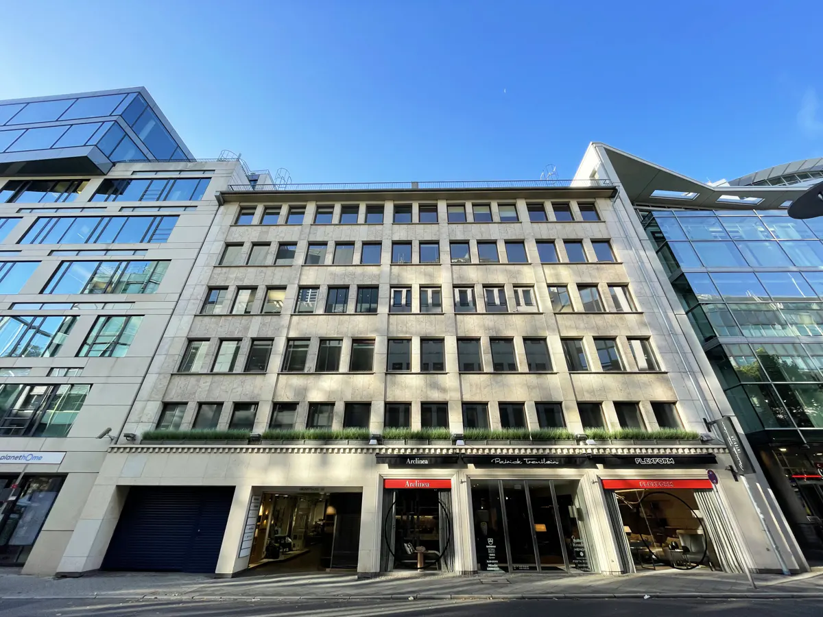 Exterior of a multi-story building with retail shops on the ground floor under a clear blue sky.