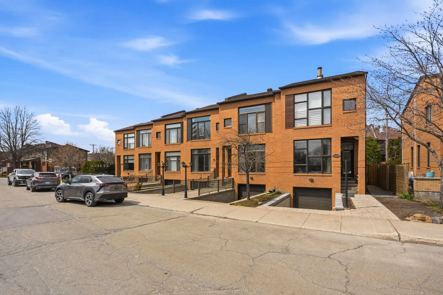 A row of three-story orange brick townhouses with black-framed windows and underground garages on a sunny day.