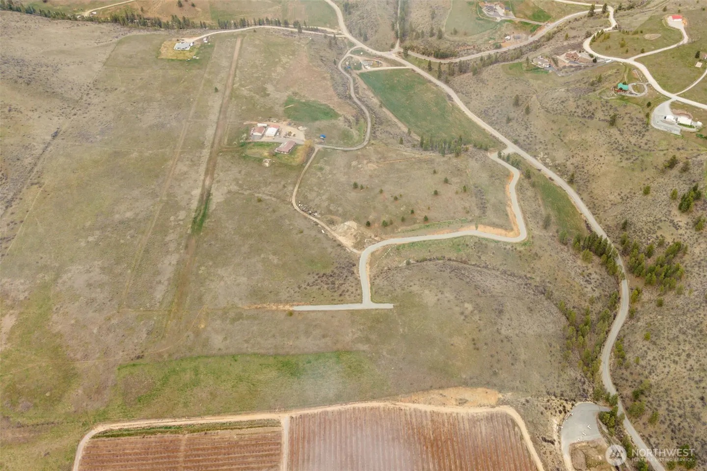 Aerial view of a large, undeveloped land parcel with a vineyard in the foreground and scattered homes in the background.