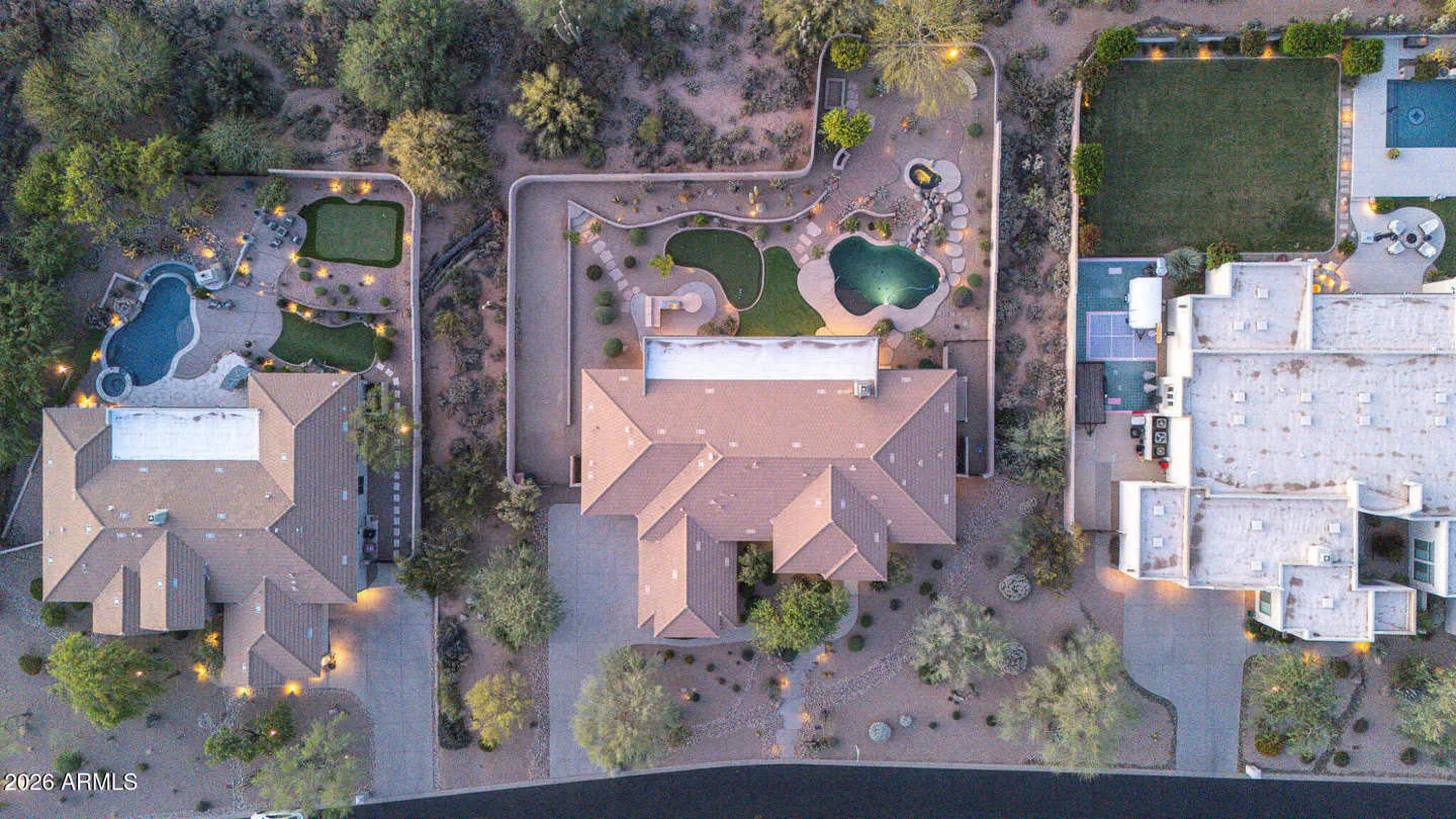 Aerial view of three luxury homes with pools, putting greens, and desert landscaping at dusk.