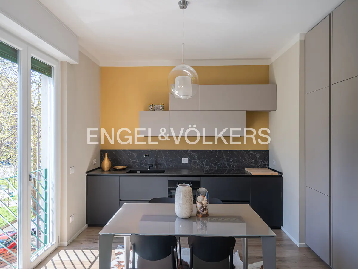 Modern kitchen with gray cabinets, black marble countertops, and a yellow accent wall. A glass table with black chairs sits in the foreground.