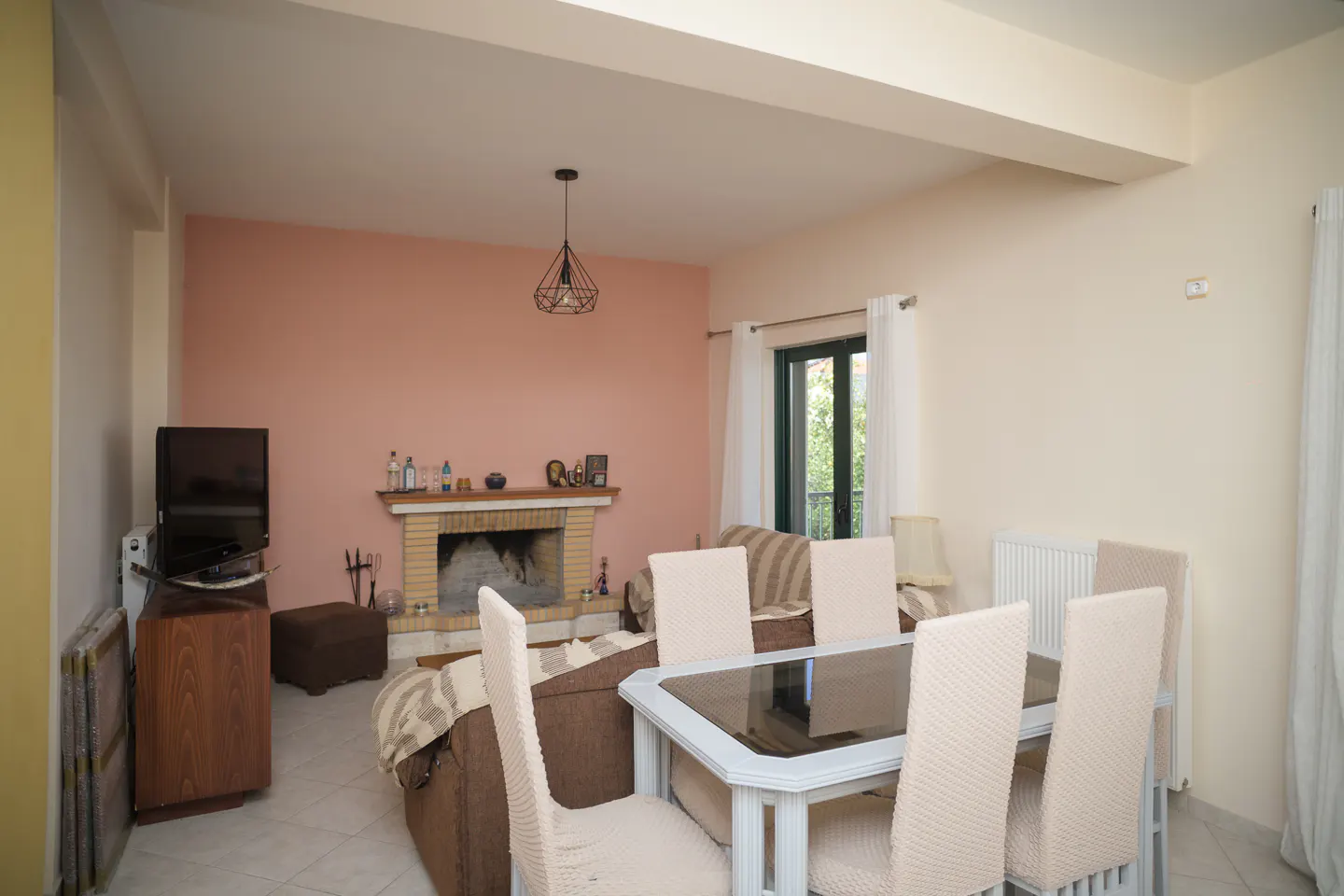 Living room with a fireplace, brown sofa, and a dining table with six chairs. A TV is on a wooden stand. The walls are painted in peach and cream colors.