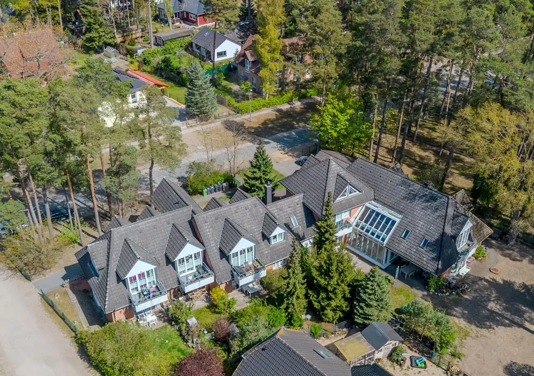 Aerial view of a multi-unit home with gray roofs, white trim, and balconies, surrounded by green trees and lawns.