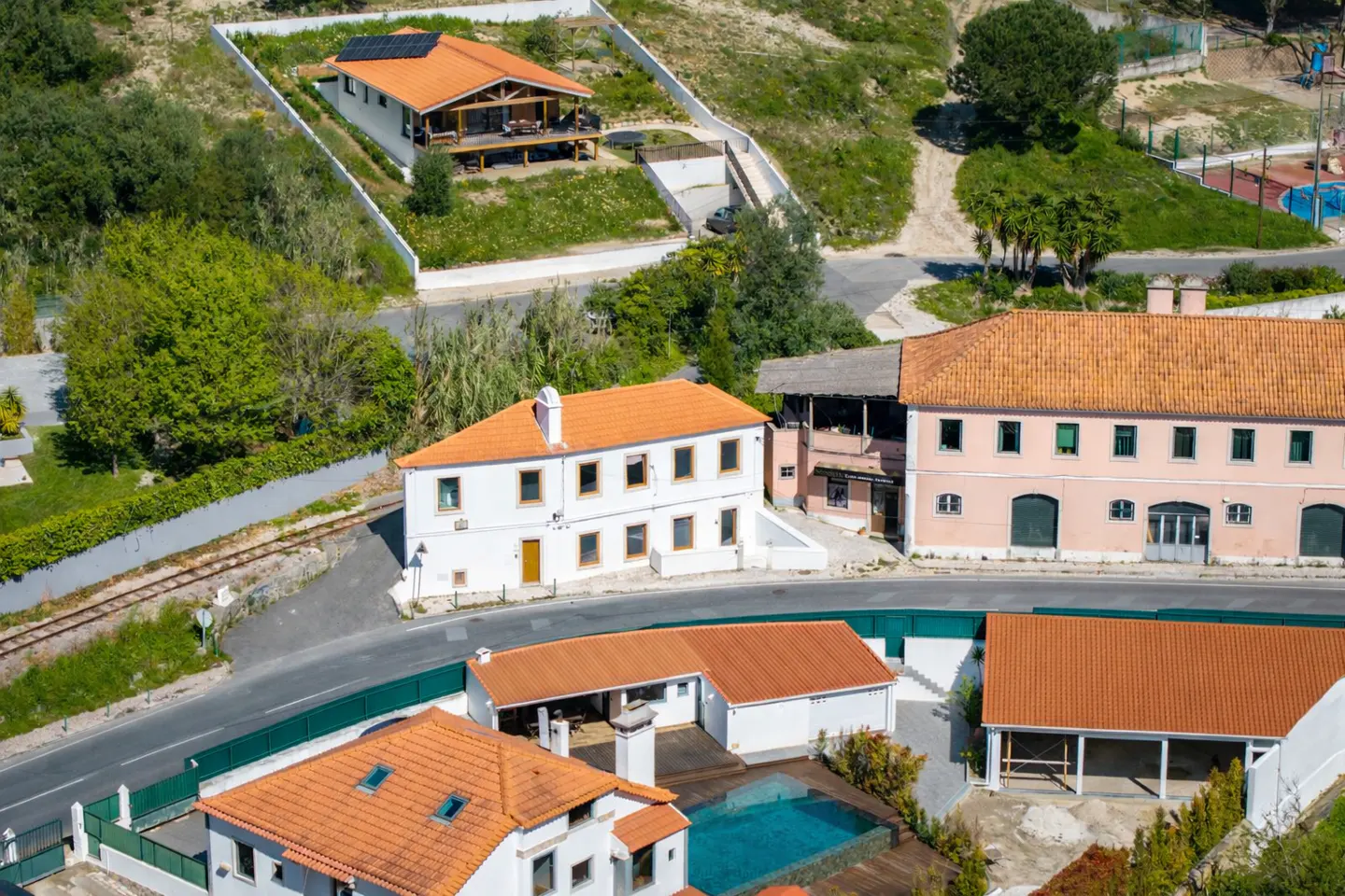 Aerial view of multiple white houses with orange tile roofs, a pool, and green trees.