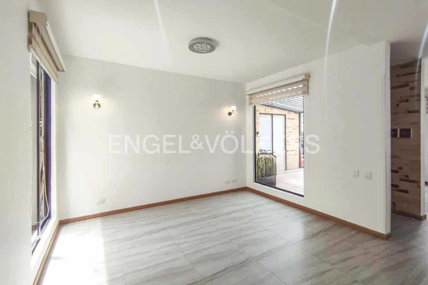 Bright, empty room with white walls, marble floors, and large windows. Engel & Völkers logo visible on the wall.