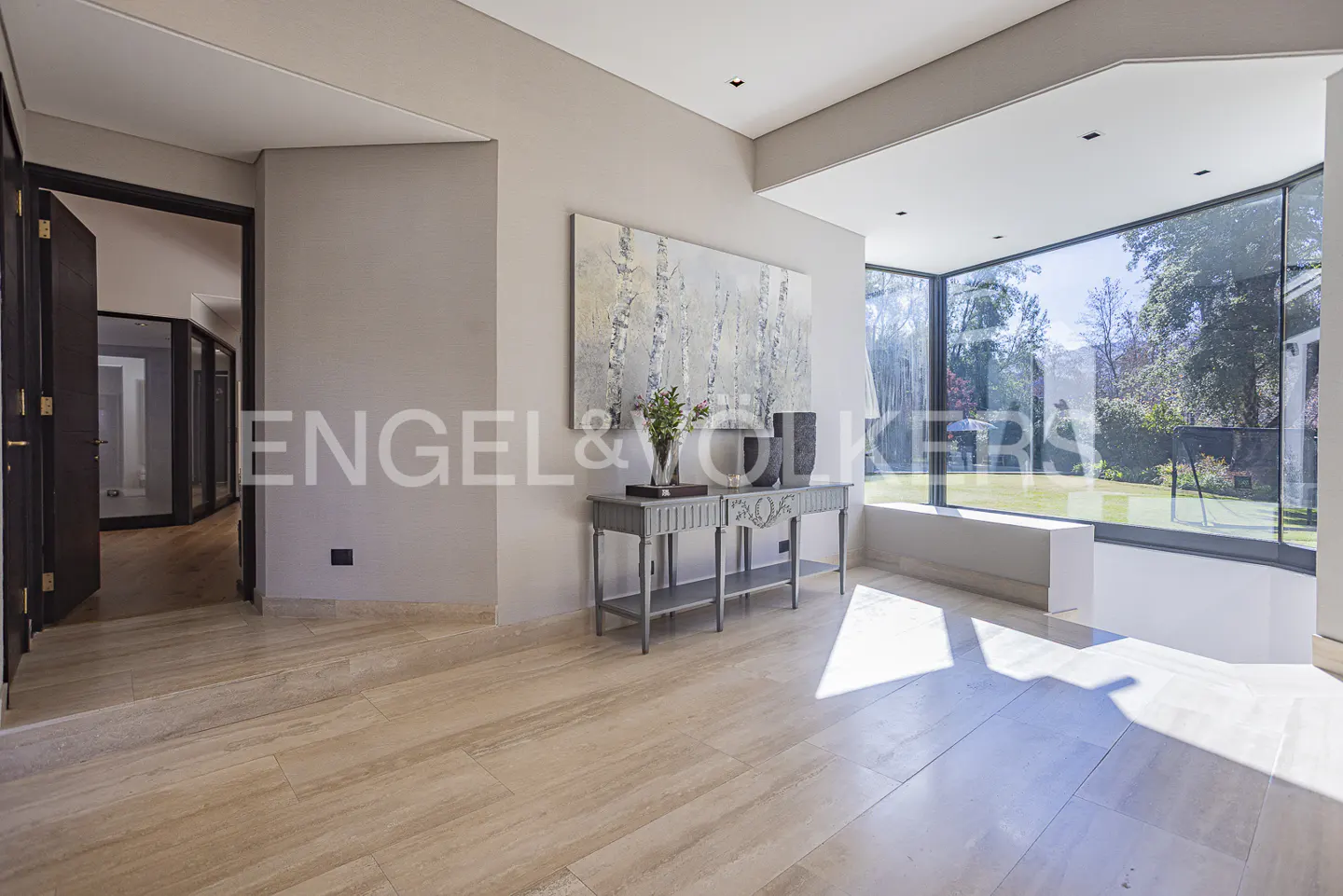 A bright foyer with beige tile floors, a gray console table with art, and a large window overlooking a green lawn.