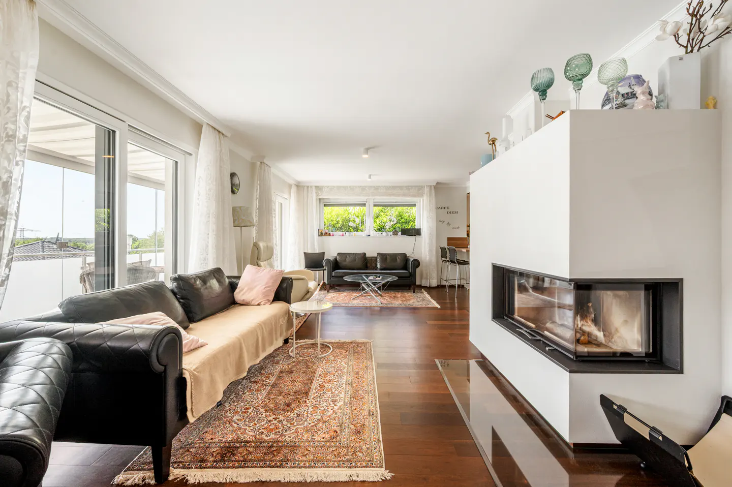 Bright living room with dark leather sofas, a modern corner fireplace, hardwood floors, and patterned area rugs.