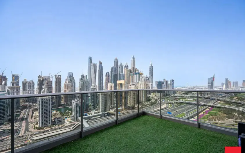 View from a balcony with green turf, overlooking the Dubai skyline and highway on a clear day.
