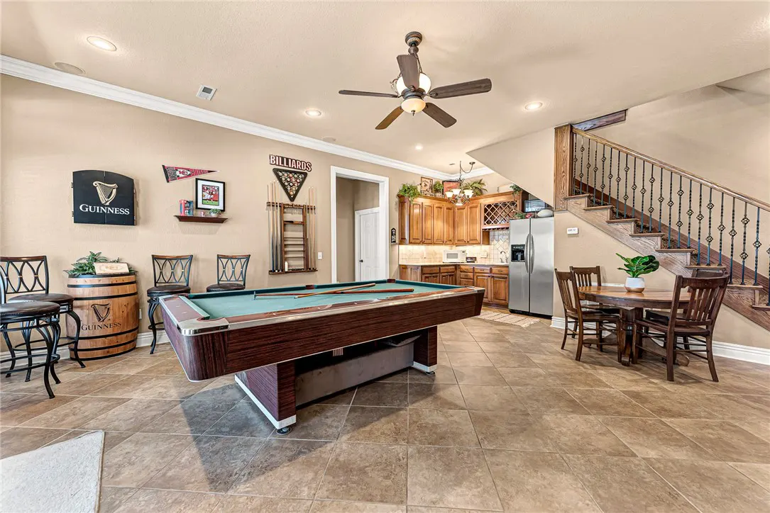 A game room with a pool table, bar stools, and a small kitchen area. Stairs lead to another level.