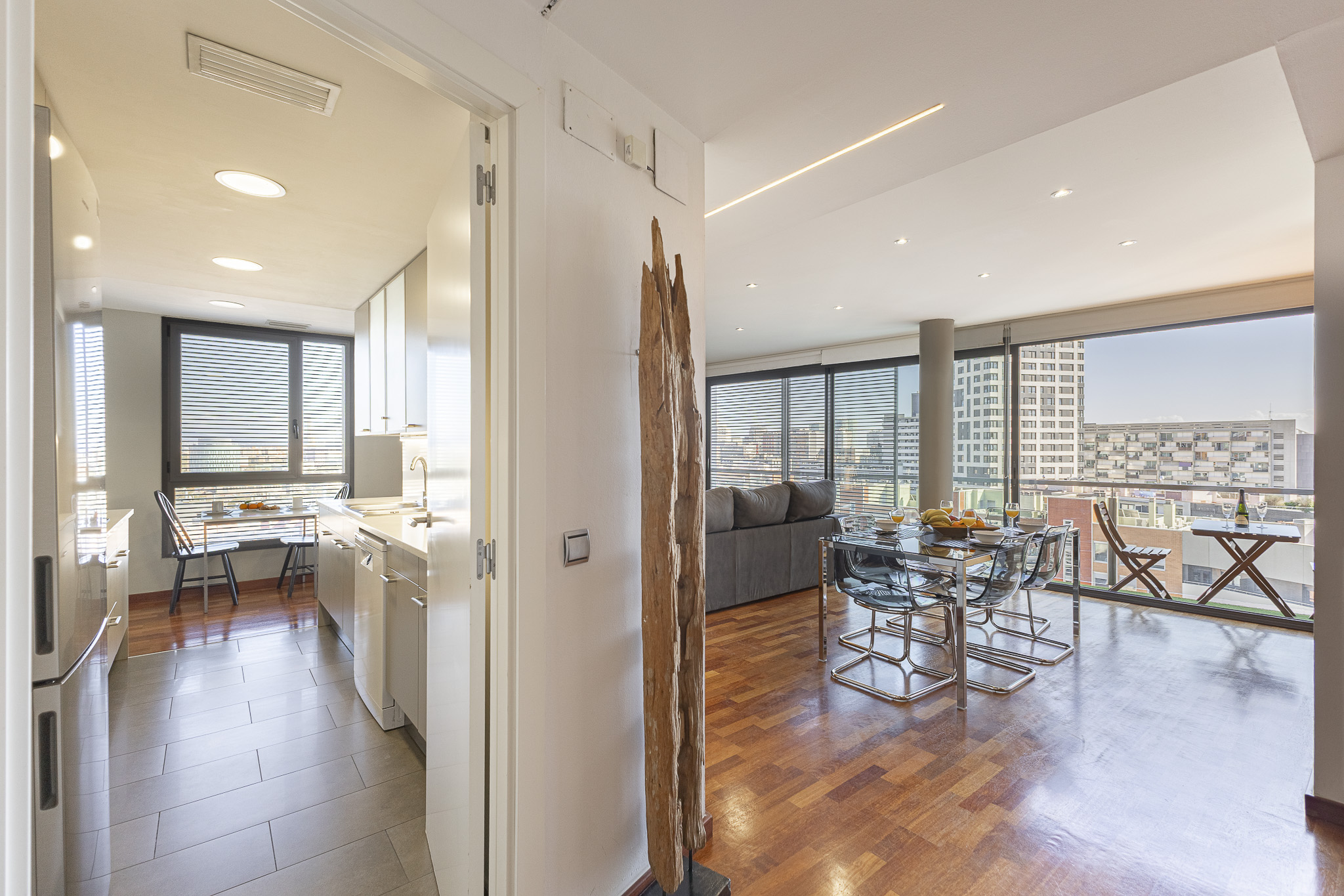Modern apartment interior with a kitchen, dining area, and living room featuring hardwood floors and floor-to-ceiling windows. [AI-generated text]