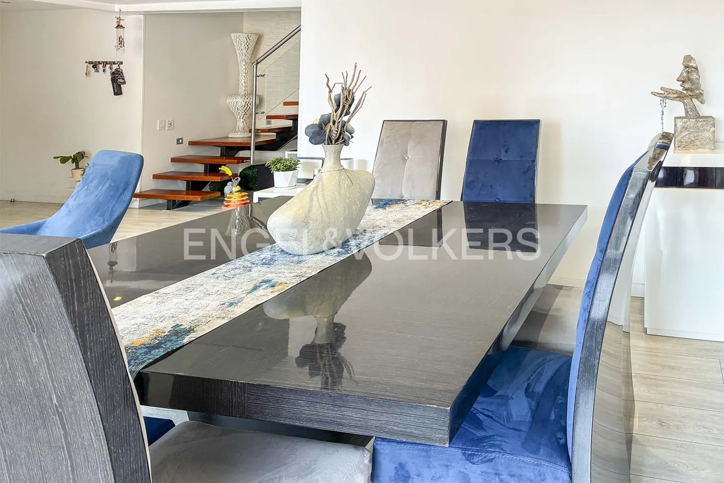 Modern dining room with a glossy black table, blue and grey upholstered chairs, and a decorative vase centerpiece.