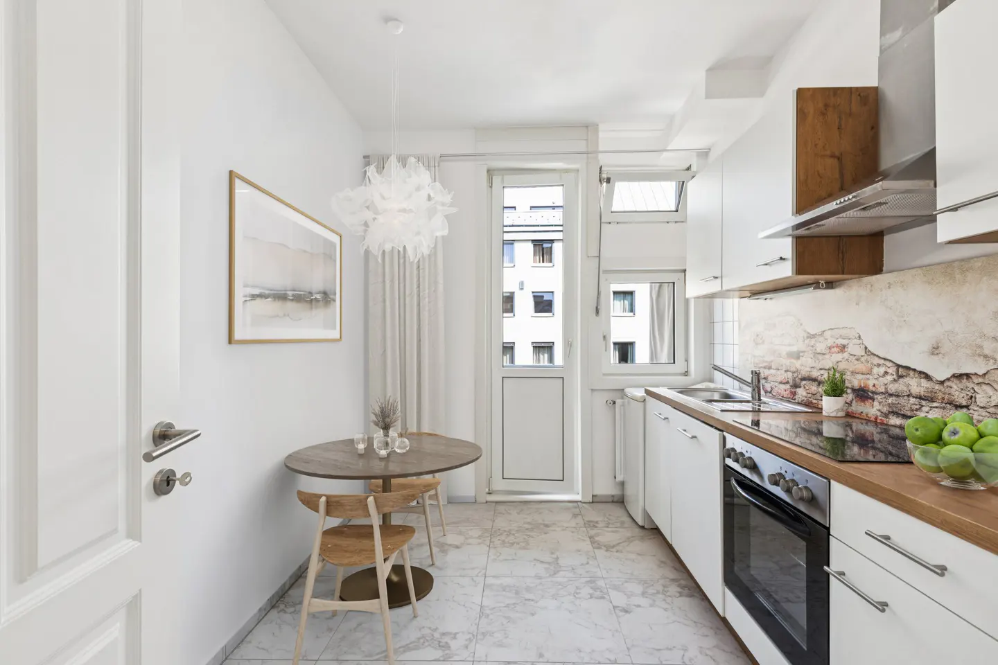 Bright kitchen with white cabinets, wood countertops, and marble floors. A round table with two chairs sits near a window.