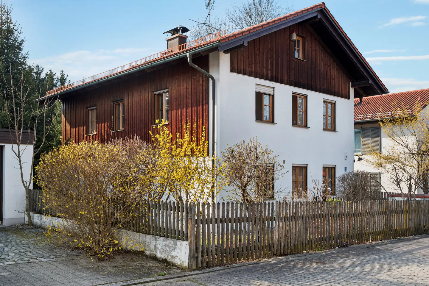 Two-story house with white and brown wood siding, a brown roof, and a wooden fence in front.