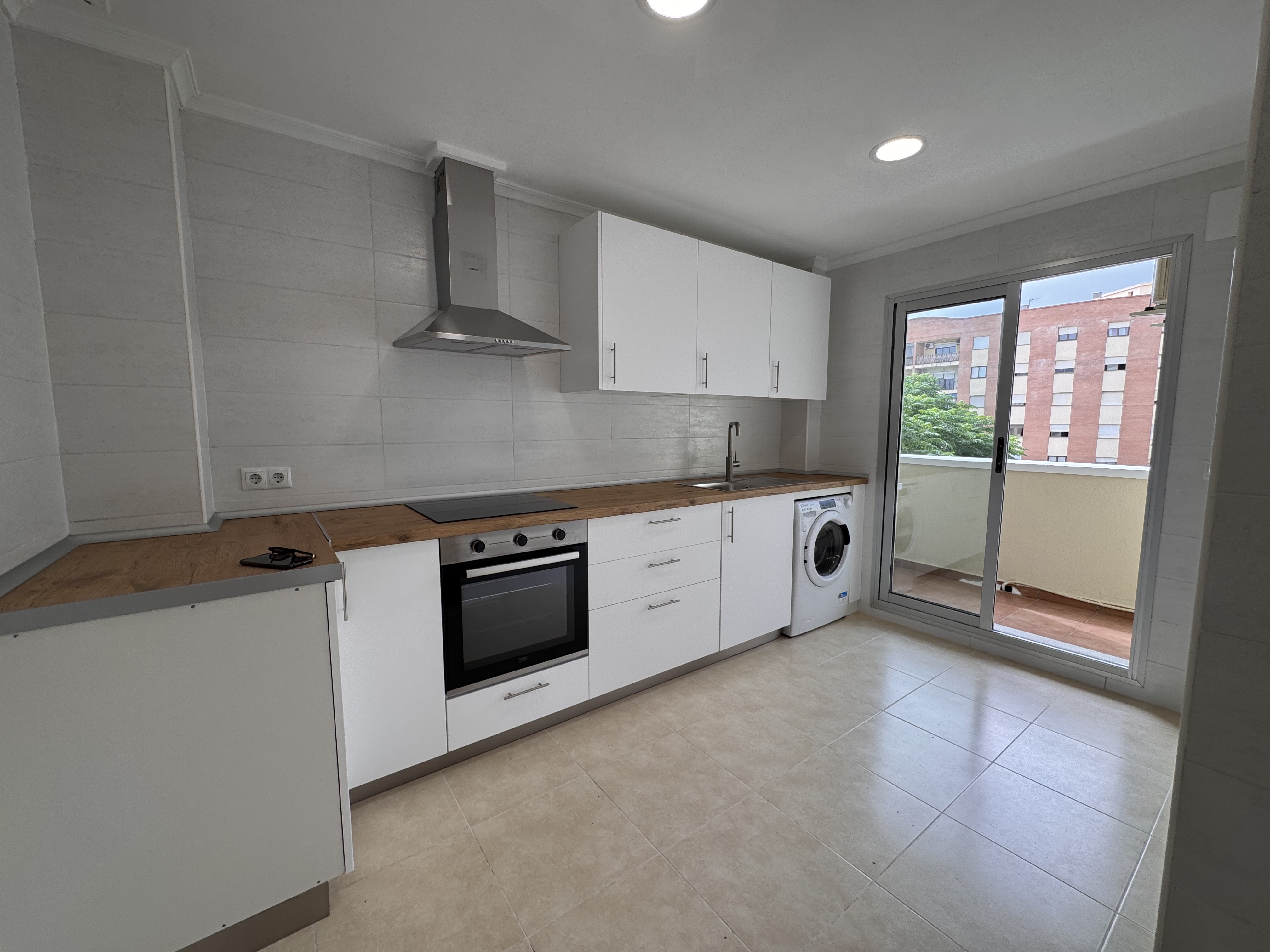 Modern kitchen with white cabinets, wood countertops, stainless steel appliances, and a sliding door to a balcony.