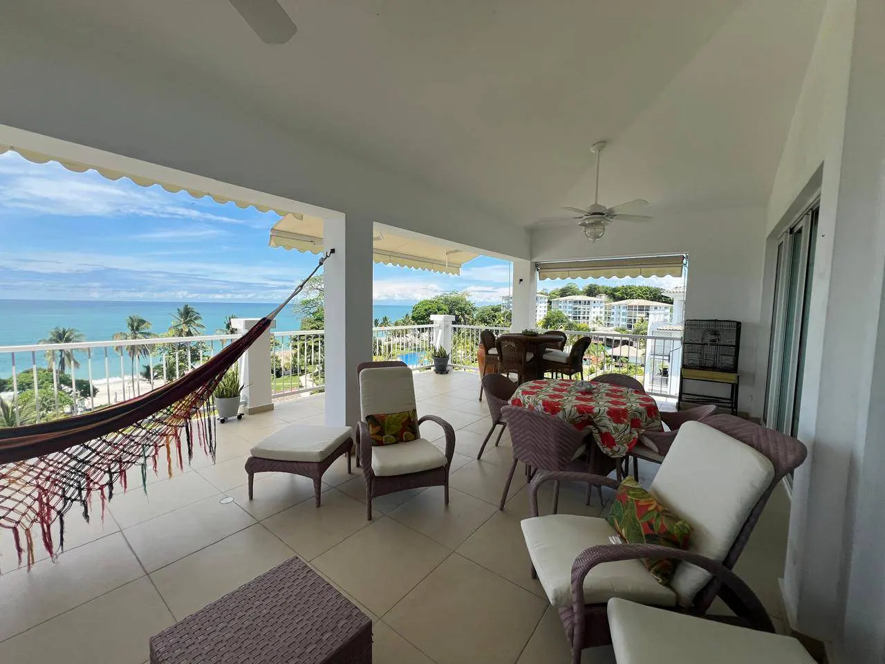 Wide shot of a covered patio with wicker furniture, a hammock, and an ocean view.