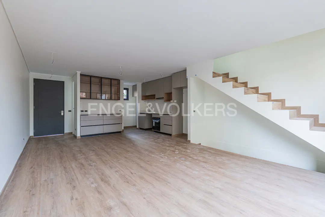 Modern open-plan living area with light wood floors, grey kitchen cabinets, and a staircase with wooden steps.