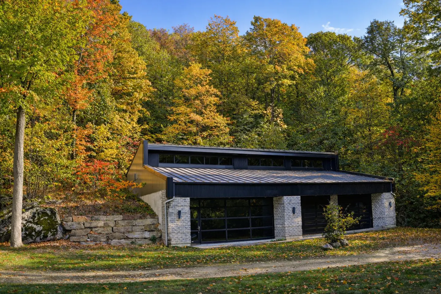 Modern garage with black trim and glass doors, nestled into a hillside with fall foliage.