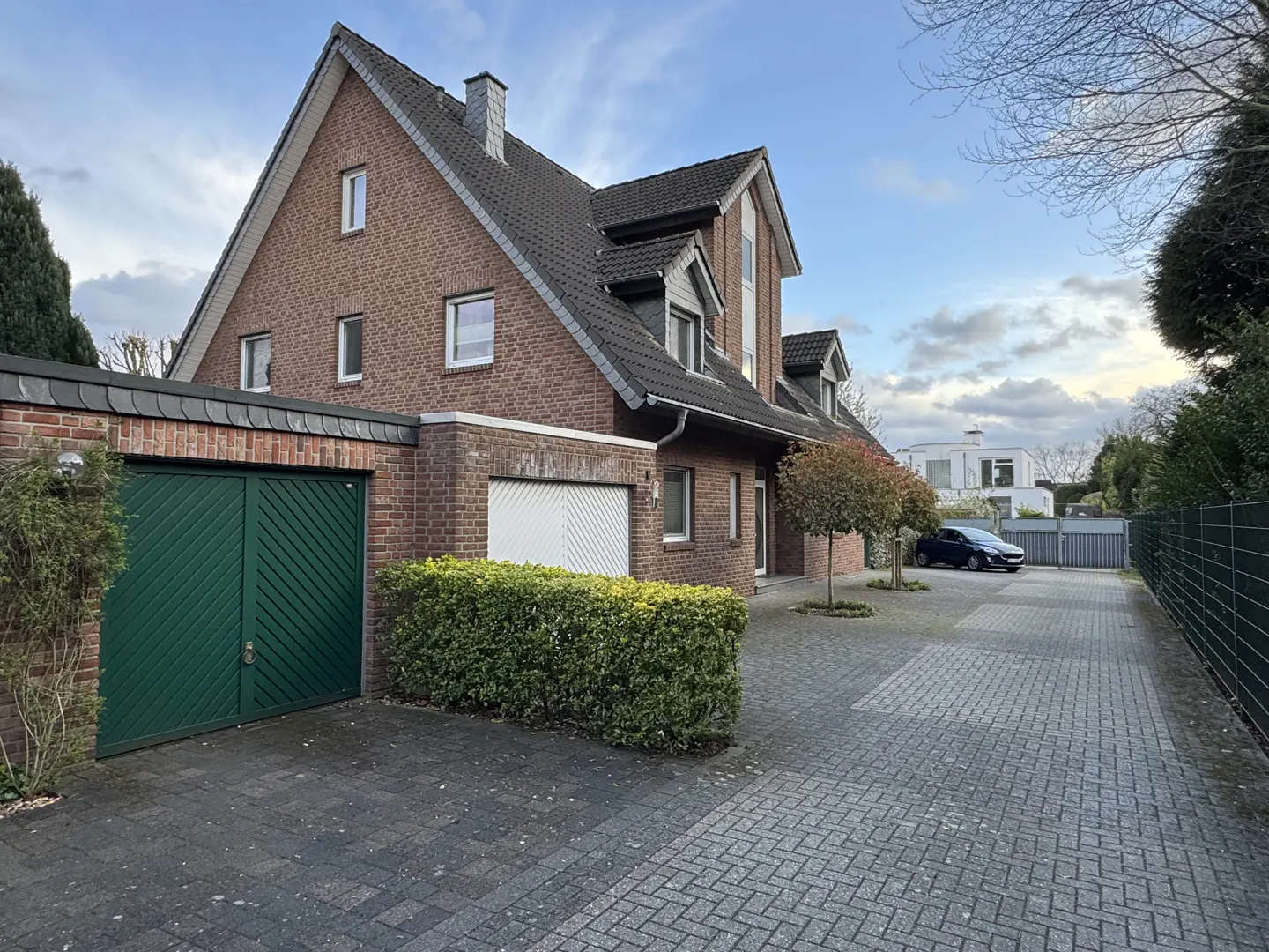 A two-story brick house with a dark gray roof, green garage door, and a paved driveway.