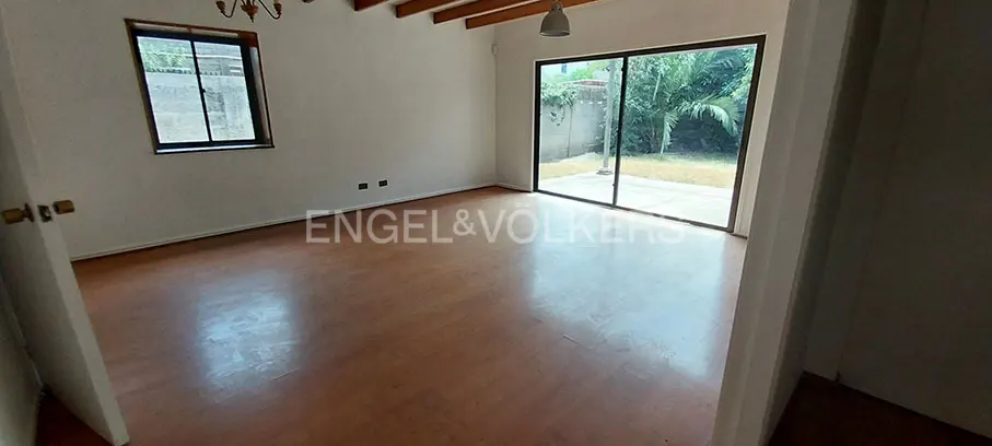 An empty room with wood floors, white walls, and a sliding glass door to a backyard with trees. A window is on the left wall.