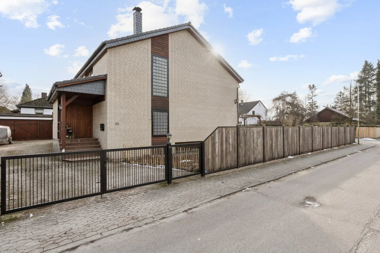 Two-story house with light brick, dark wood trim, and a black metal fence. A wooden fence runs along the side of the property.