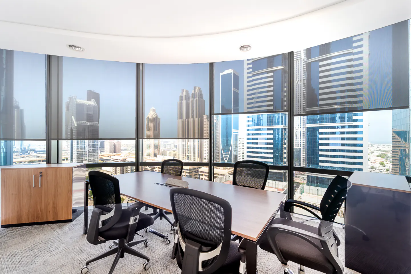 Conference room with a large table, black chairs, and a panoramic view of a city skyline.