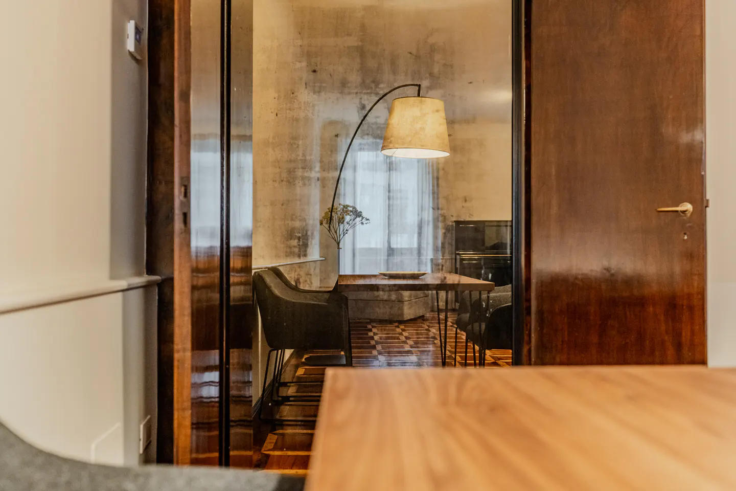 View through a doorway into a dining room with a wooden table, dark chairs, and a tall arched floor lamp.
