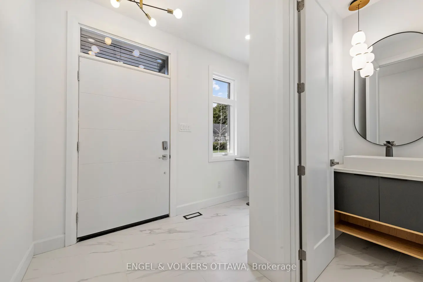 Bright, modern entryway with a white door, marble floors, and a glimpse of a bathroom with a round mirror and vanity.
