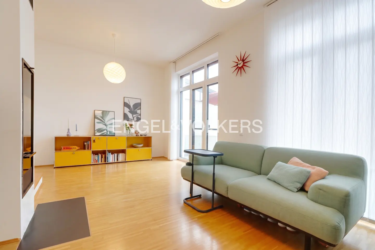 Bright living room with wood floors, a light green sofa, and a yellow cabinet against a white wall. A black side table sits next to the sofa.