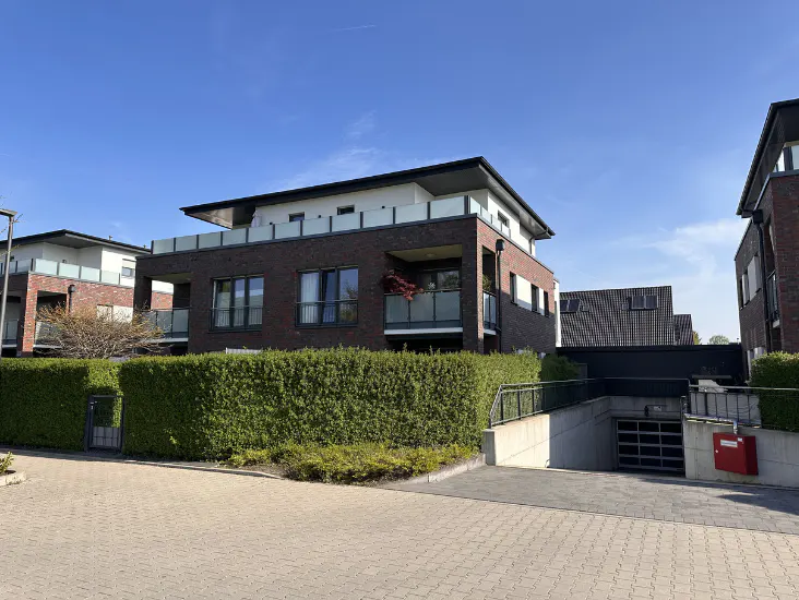 Modern brick apartment building with a balcony and underground parking on a sunny day.