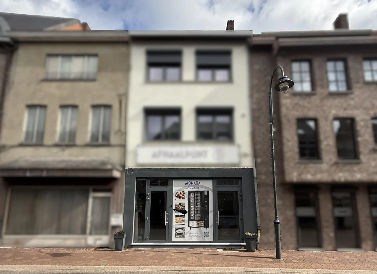 Exterior view of a Monaxa food vending machine shop in a row of buildings on a brick sidewalk.