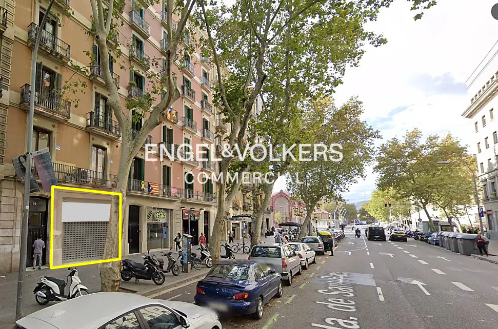 Commercial property with a closed metal shutter, outlined in yellow, on a city street with parked cars and trees.