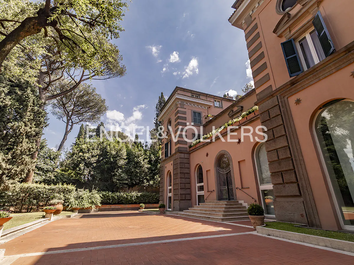 A salmon-colored villa with stone accents, arched doorways, and a large terracotta patio under a bright blue sky.